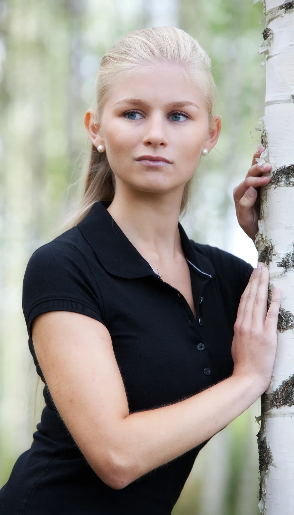 Emily standing outdoors, leaning against a birch tree, wearing a black polo shirt.