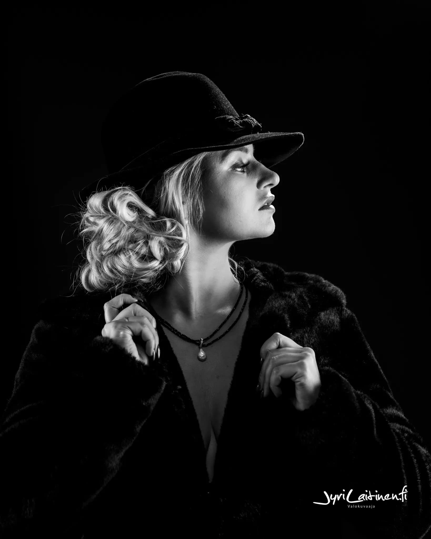 Emily wearing a hat and fur coat, looking to the side in a black and white portrait.