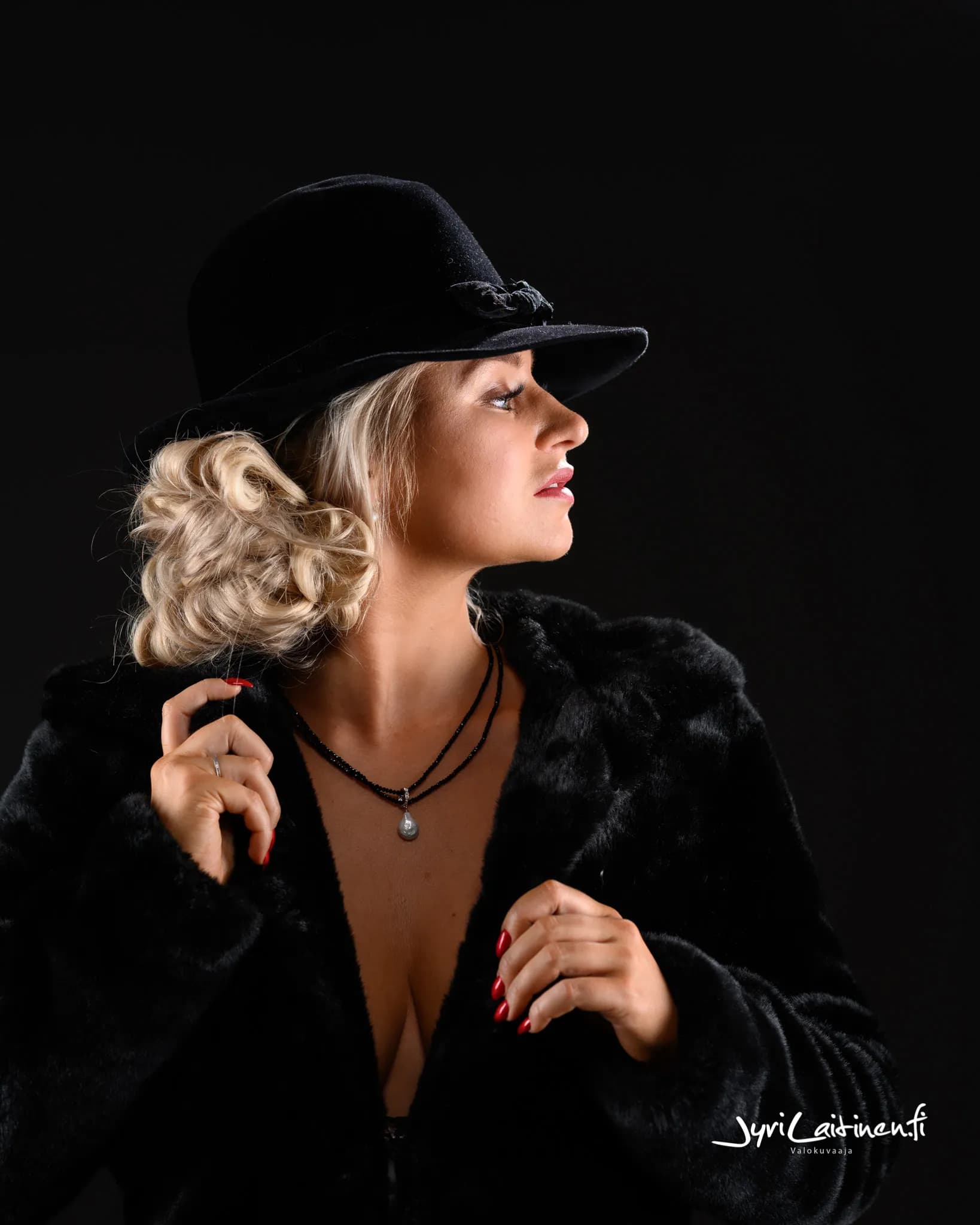 Emily wearing a black hat and fur coat, looking to the side.