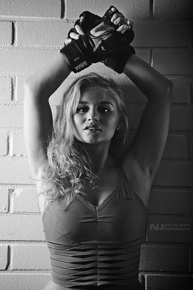 Emily posing against a brick wall wearing boxing gloves.