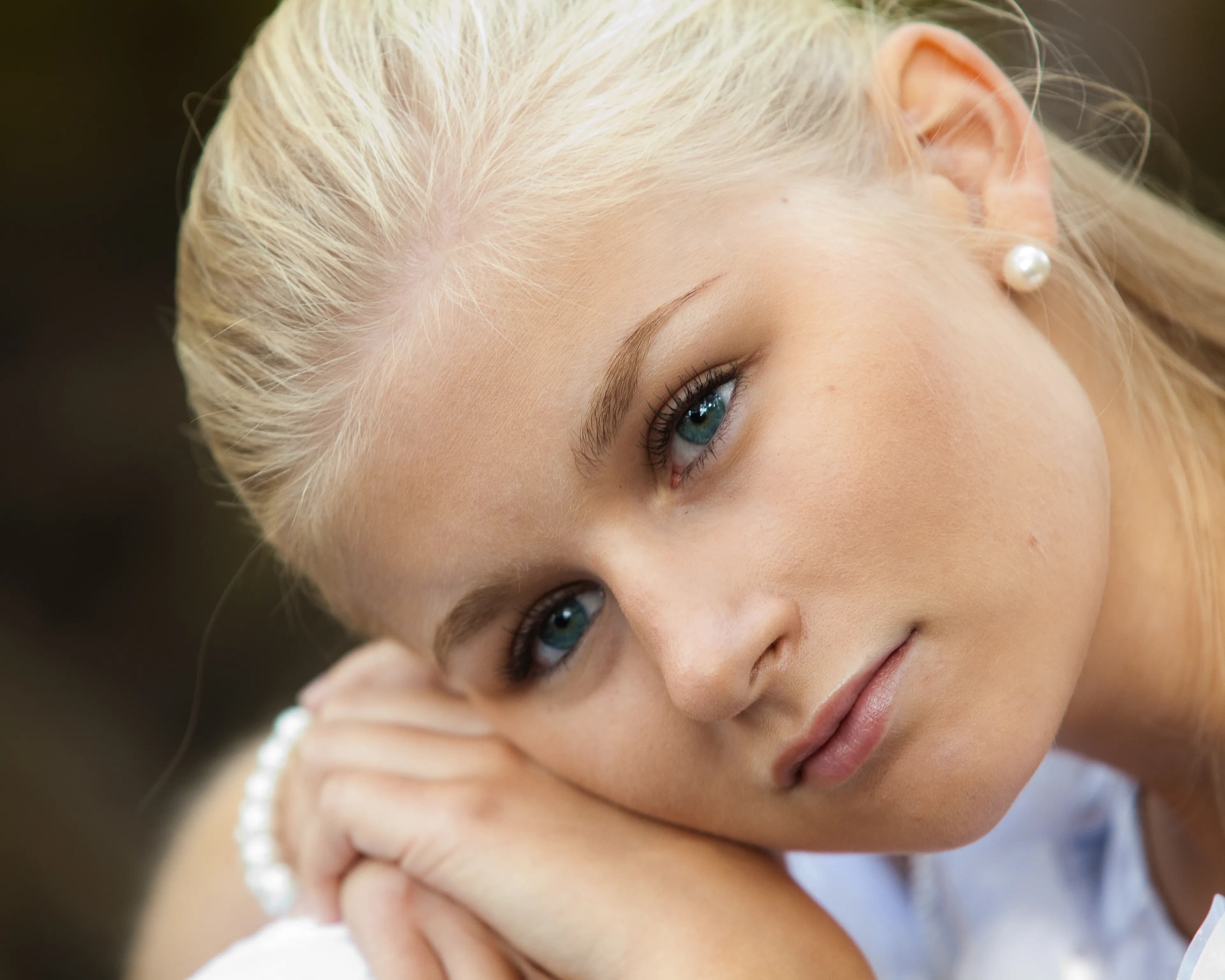 Emily with blonde hair, resting her head on her hands, wearing pearl earrings.