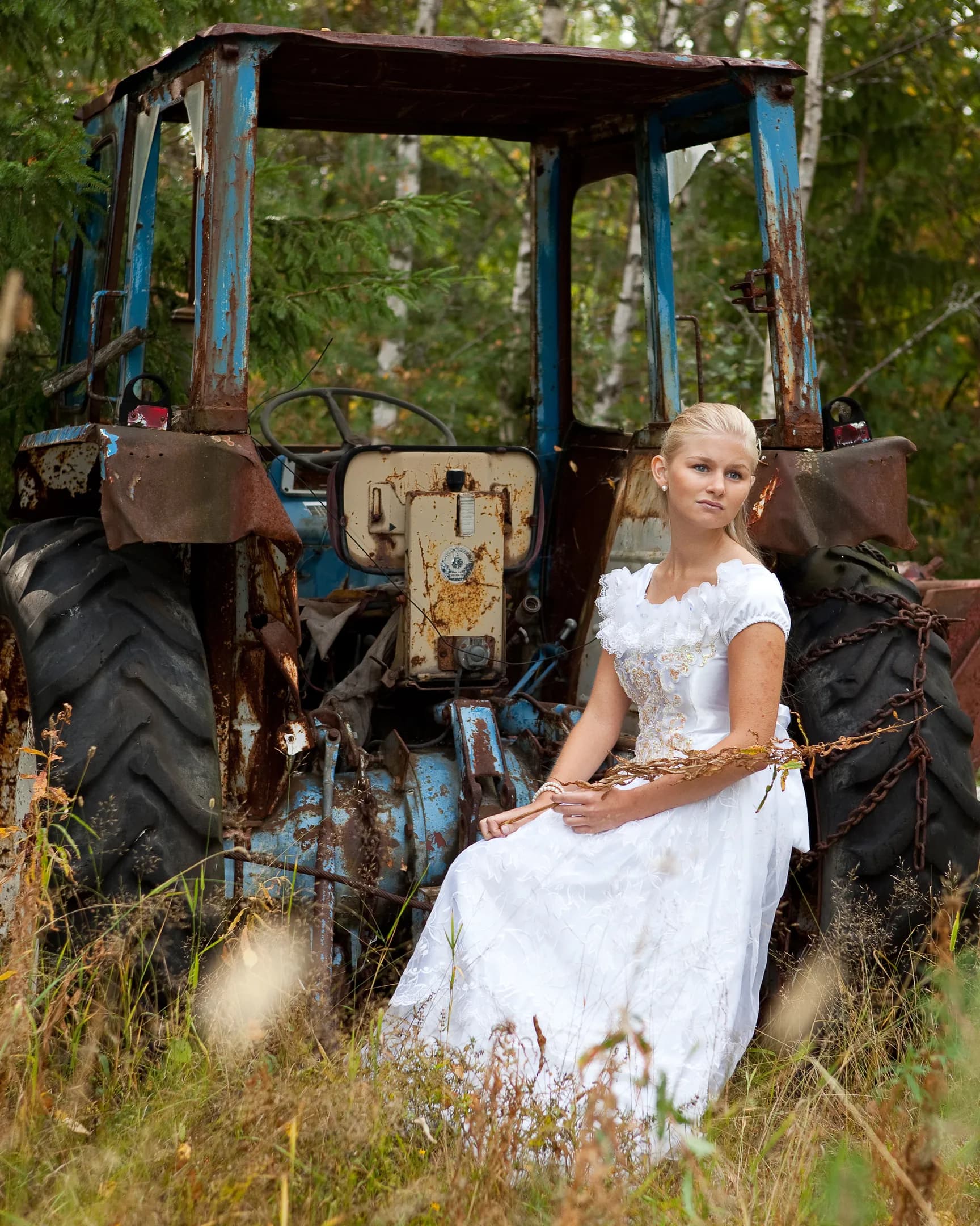 Emily in a white dress sitting on an old, rustic tractor in a field.
