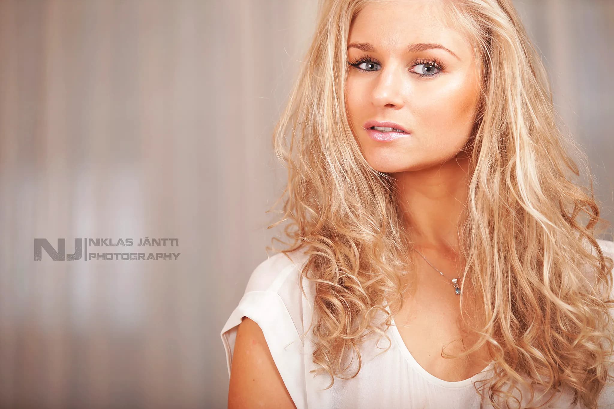Emily with long, wavy blonde hair and a white top, posing against a soft background.