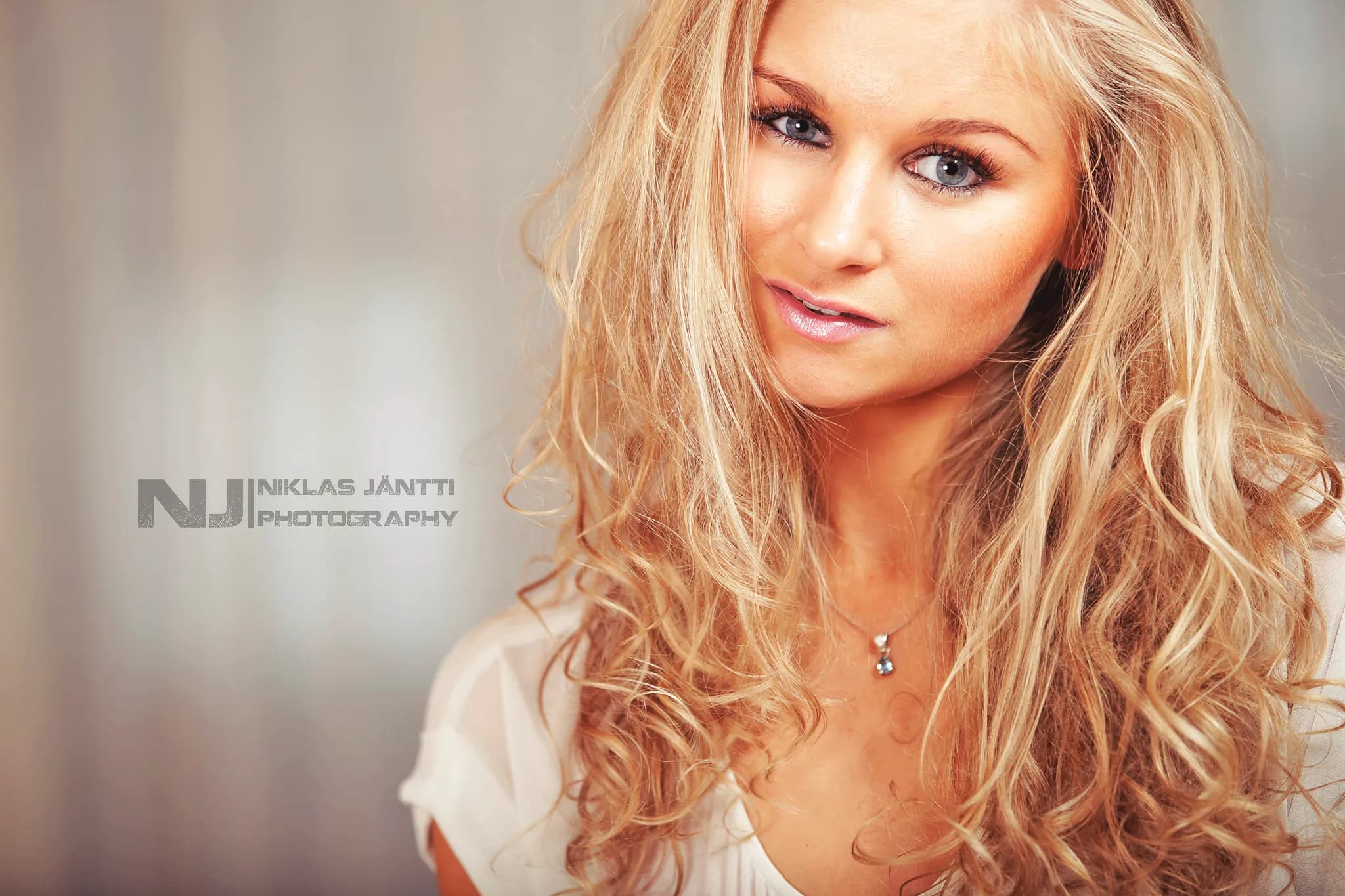 Emily with long, wavy blonde hair and a soft smile, wearing a white top.