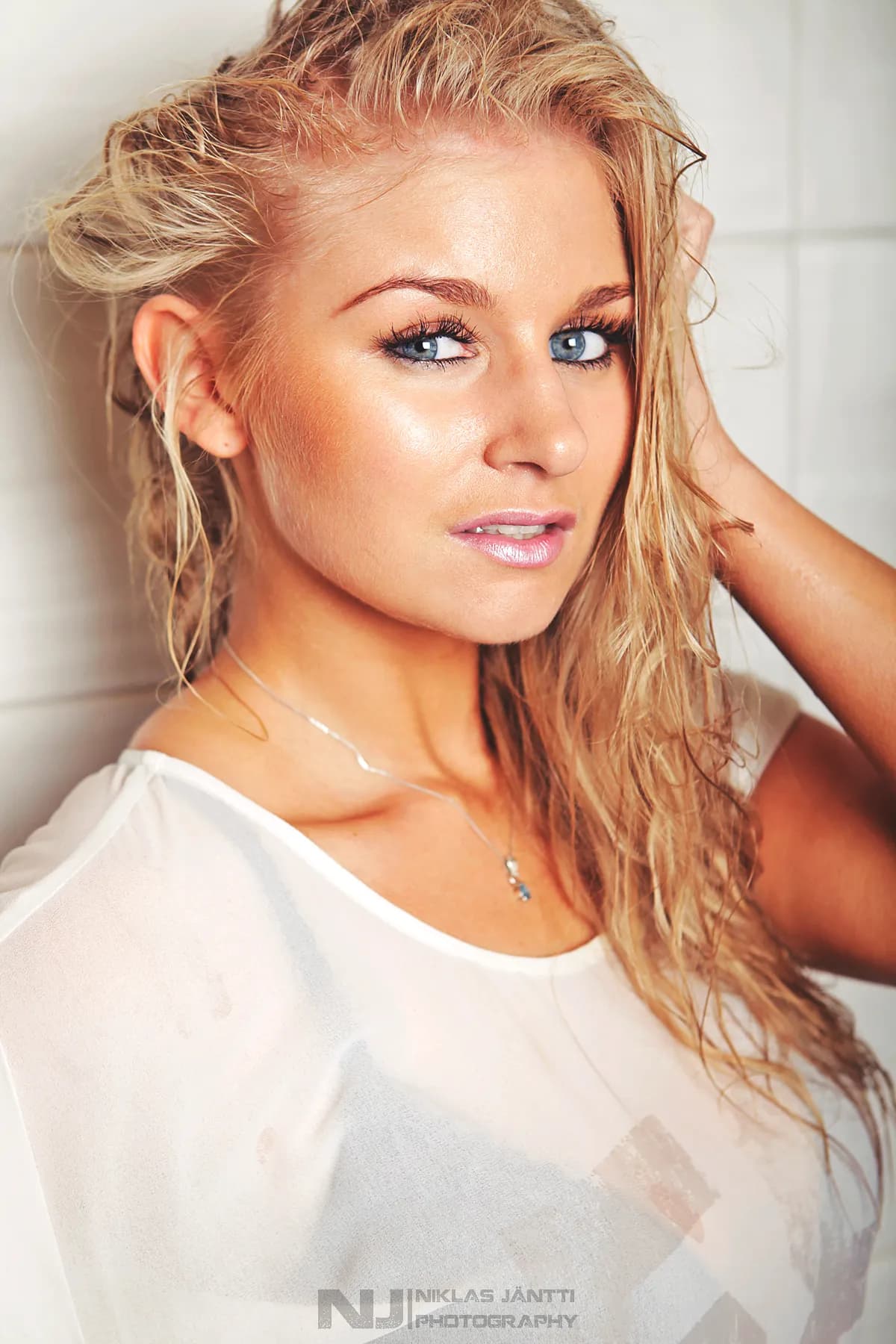 Emily with wet hair, wearing a sheer white top, posing confidently.