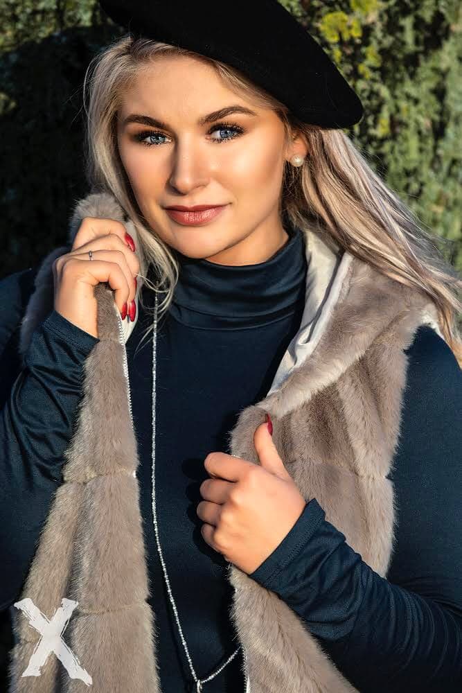 Emily wearing a black beret and a fur vest, posing outdoors.