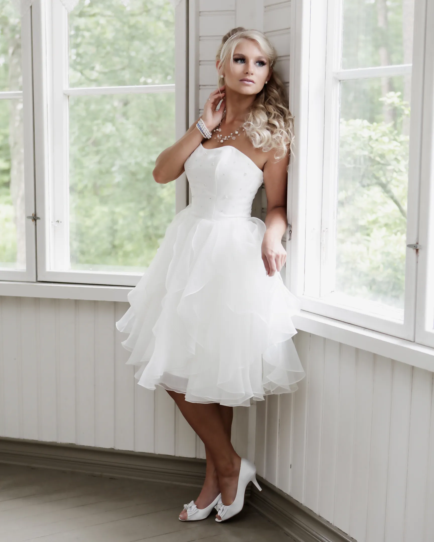 Emily in a white strapless dress standing by a window.