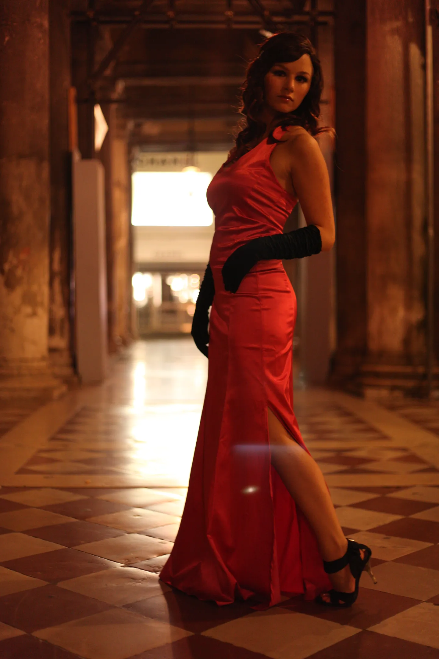 Emily in a long red evening gown posing in a dimly lit hallway.