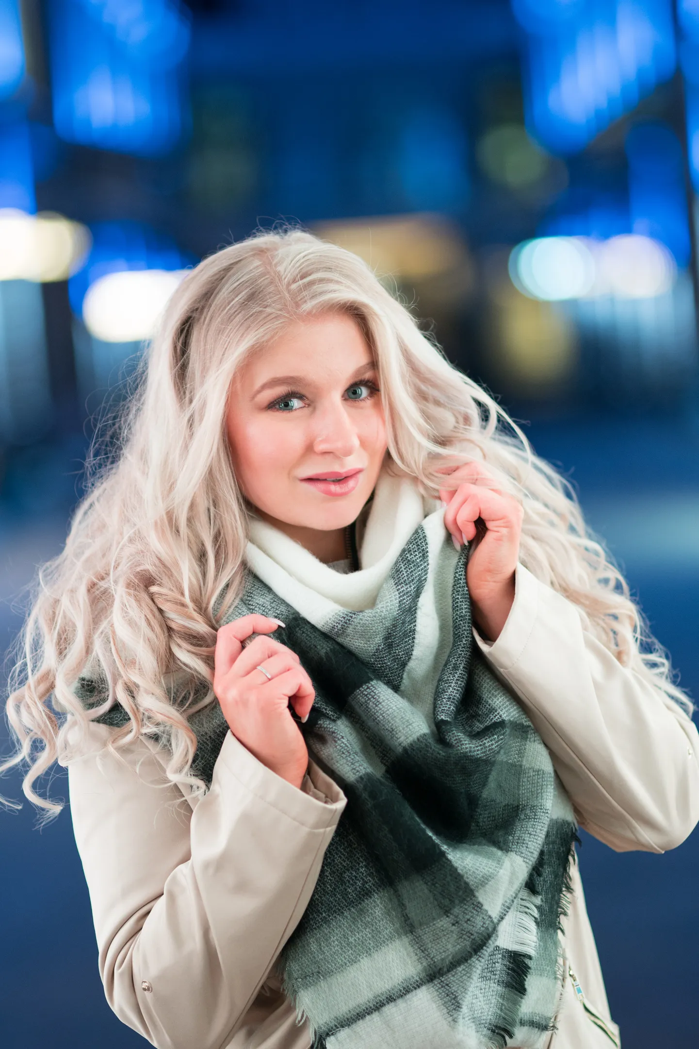 Emily with long blonde hair, wearing a scarf and coat, in a city setting at night.