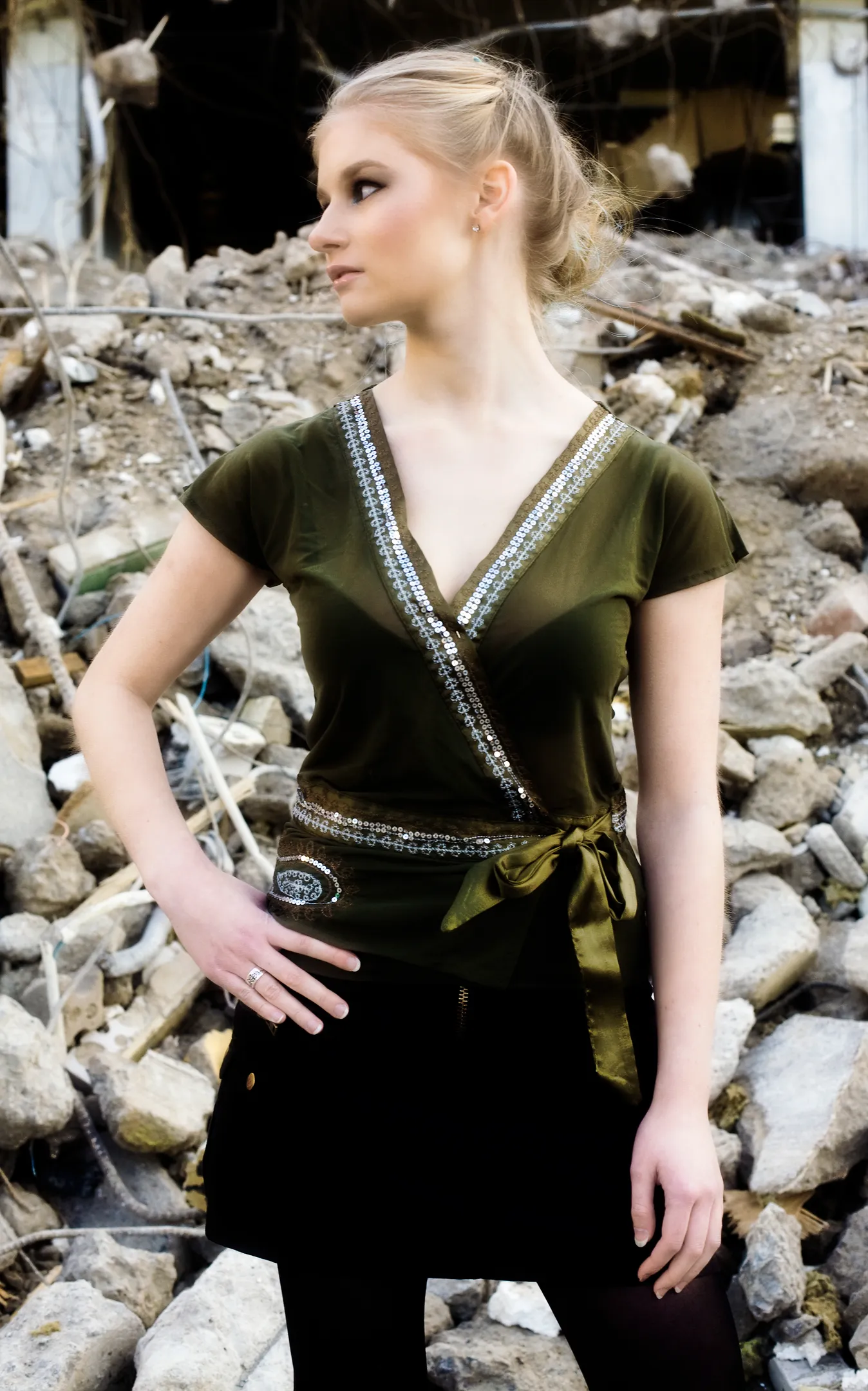 Emily standing in front of a pile of rubble, wearing a green top and black skirt.
