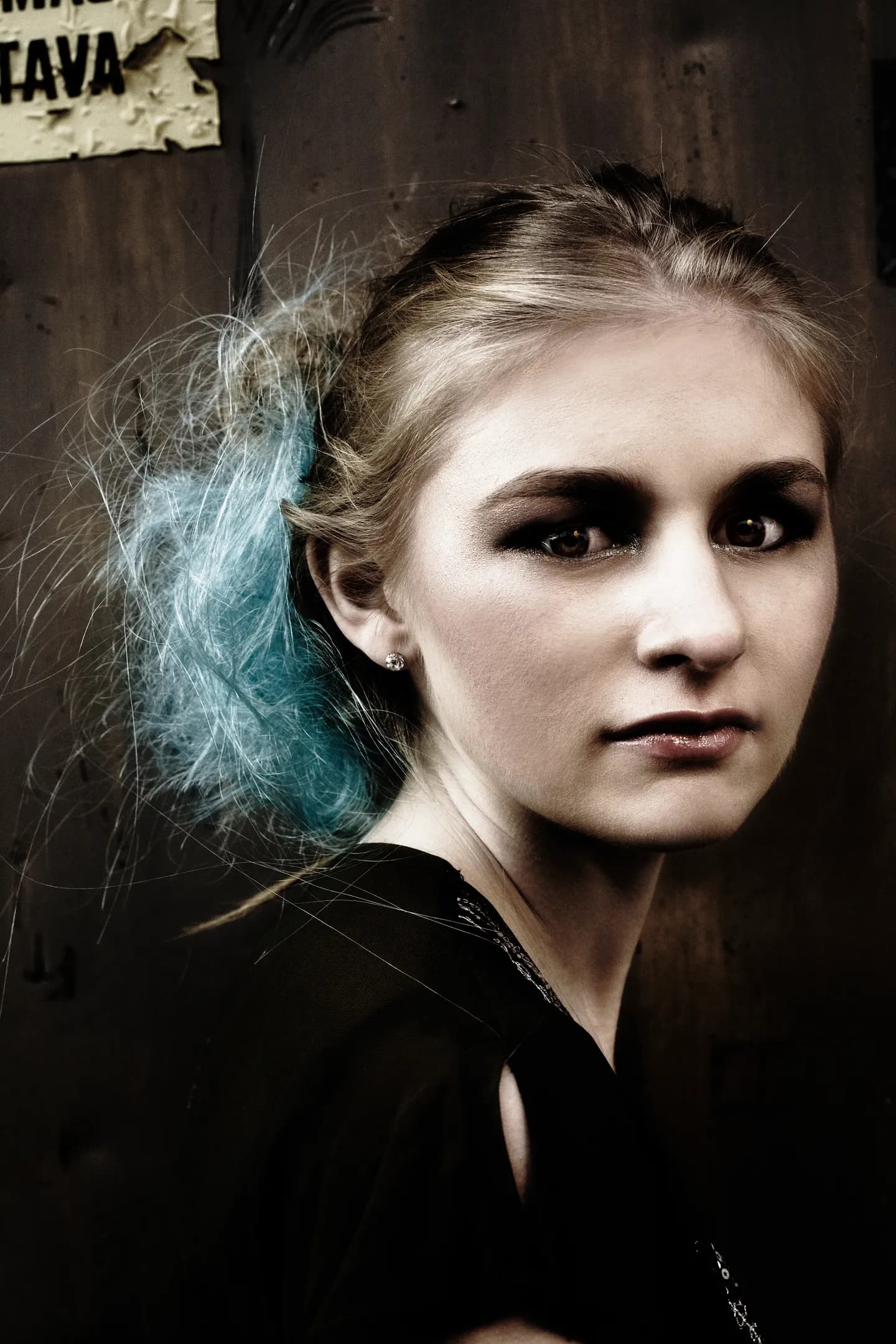 Emily with blue hair highlights, wearing a black top, poses against a dark background.