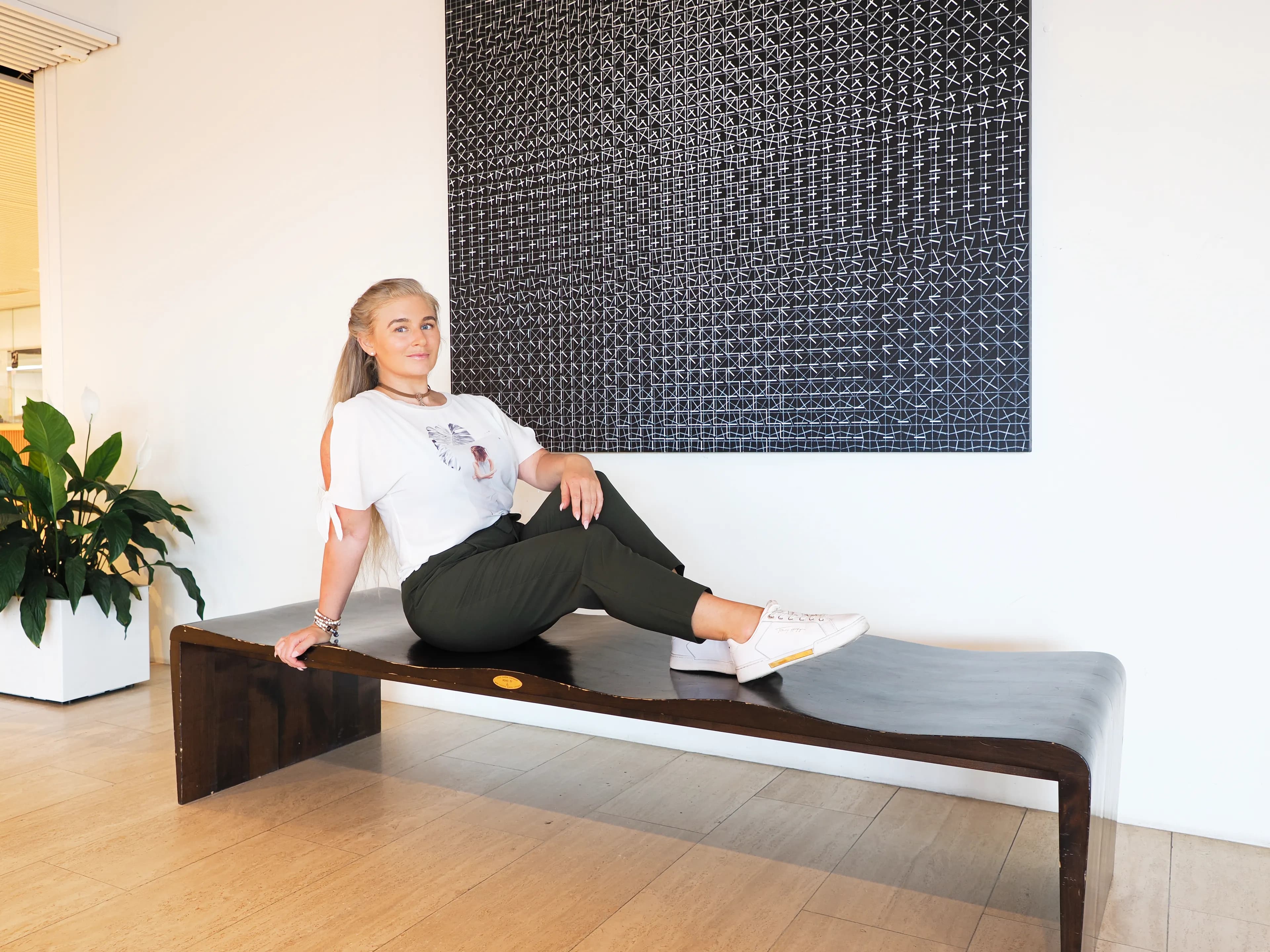 Emily sitting on a modern bench in a stylish room with a geometric artwork on the wall.