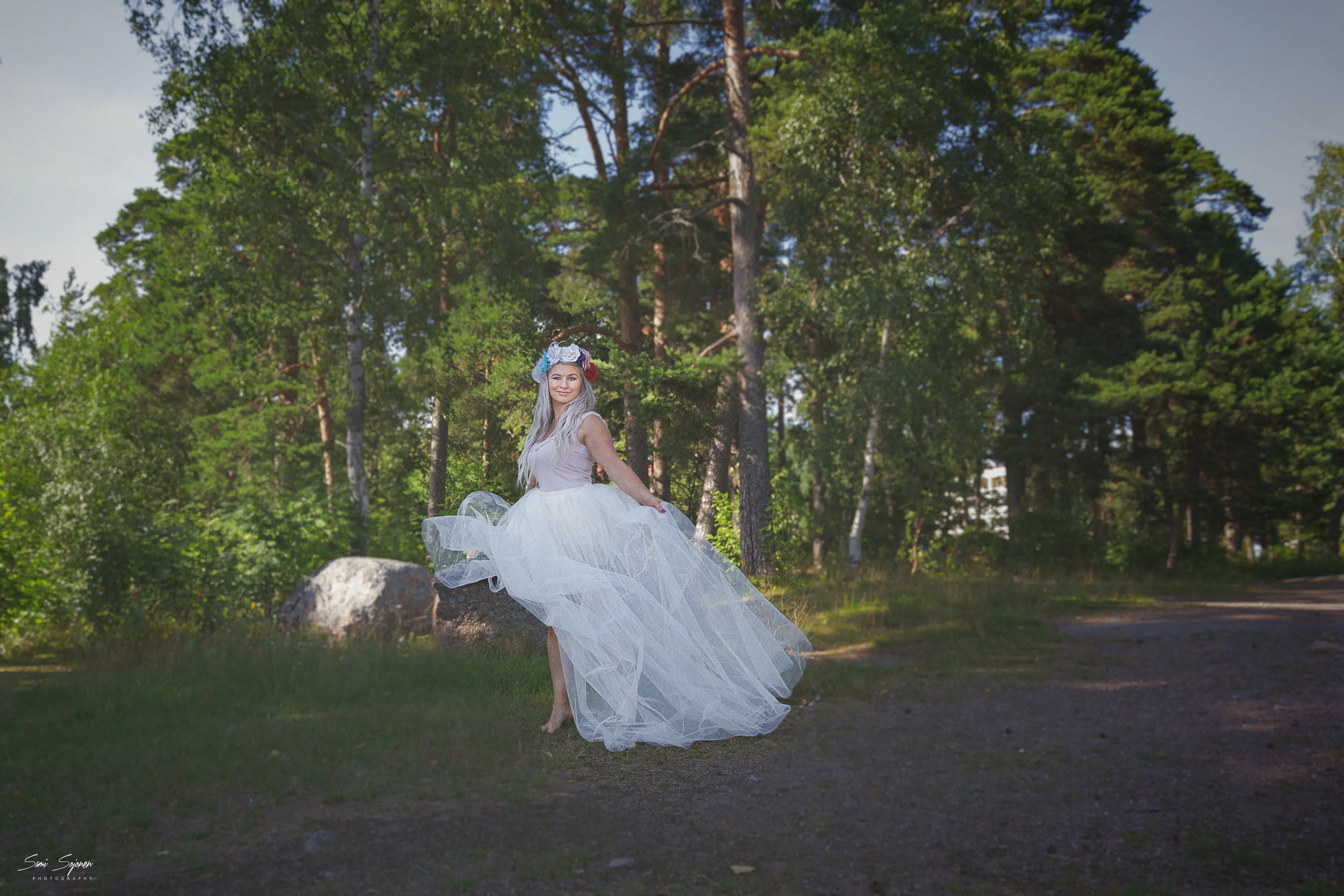 Emily in a flowing white dress and floral headpiece, standing in a forest clearing.