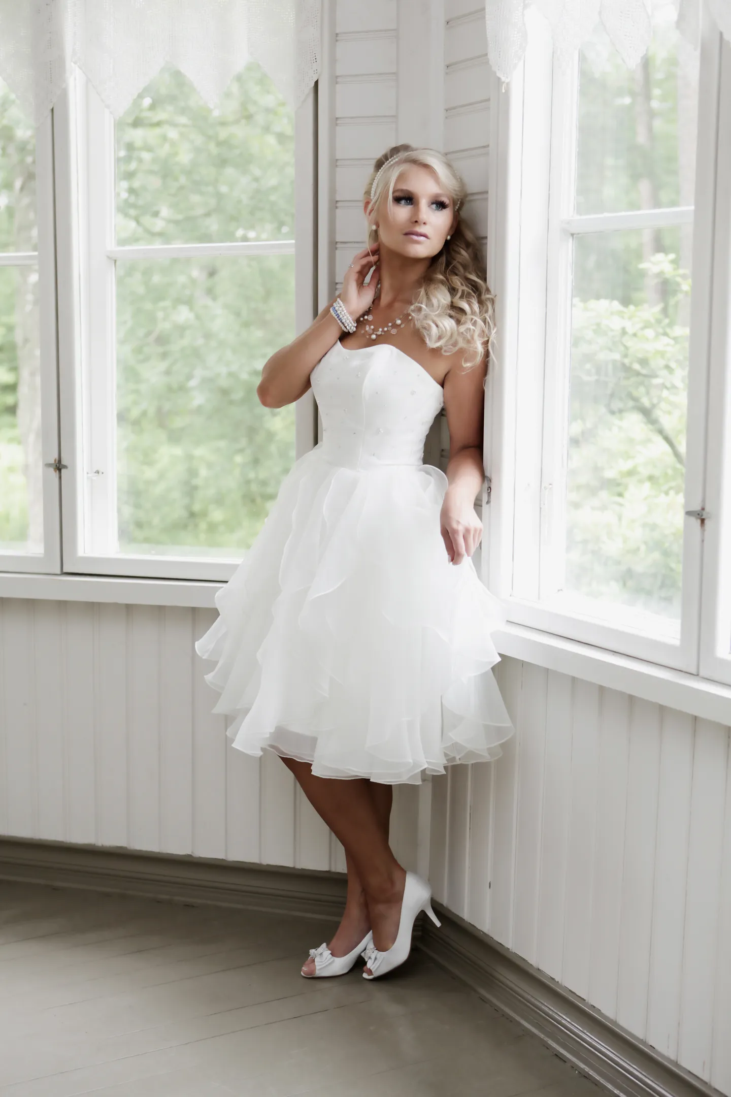 Emily in a white strapless dress posing by a window.