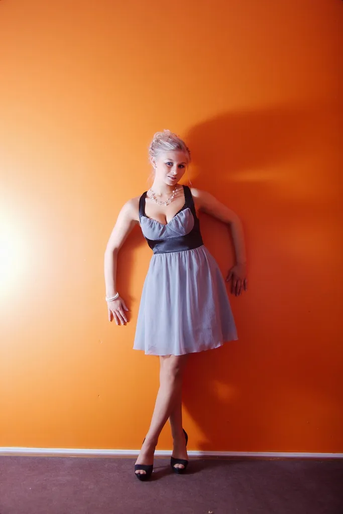 Emily posing against an orange wall in a light blue dress.