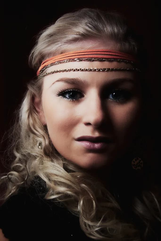 Emily with wavy blonde hair, wearing a headband and dark makeup.