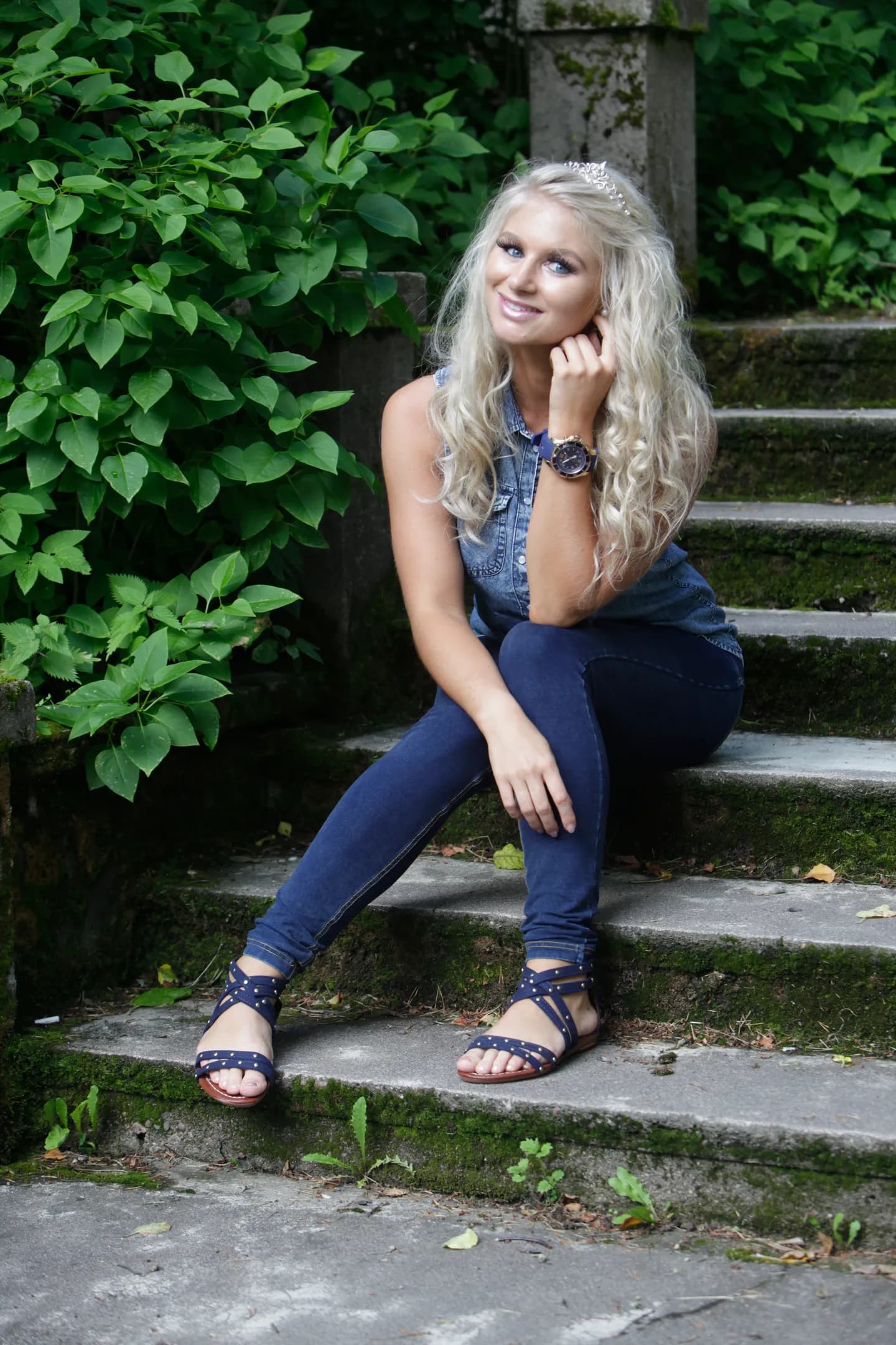 Emily sitting on outdoor steps, wearing a denim outfit and sandals, with long blonde hair.