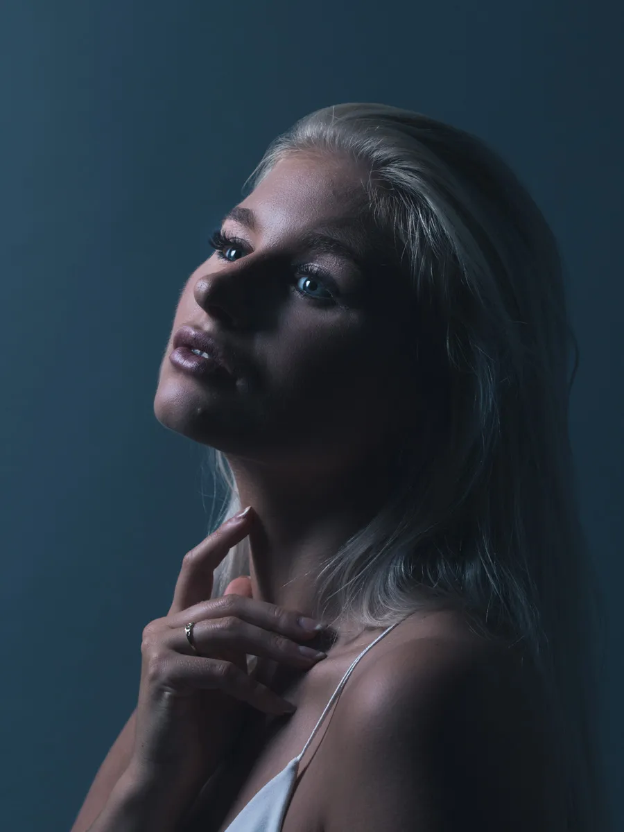 Emily posing in a dramatic, low-light setting with a thoughtful expression.