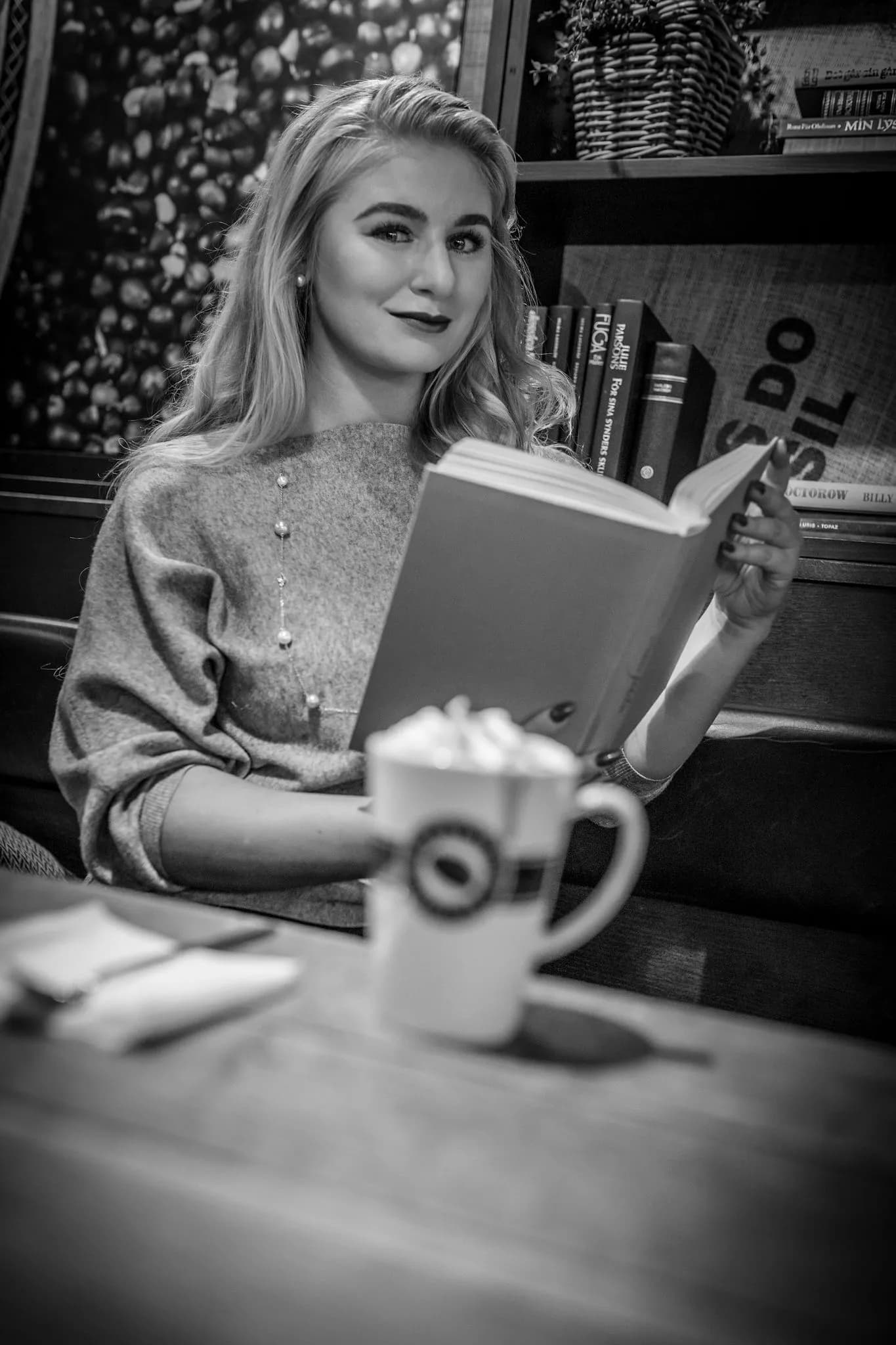 Emily sitting in a cozy cafe, reading a book with a cup of coffee on the table.