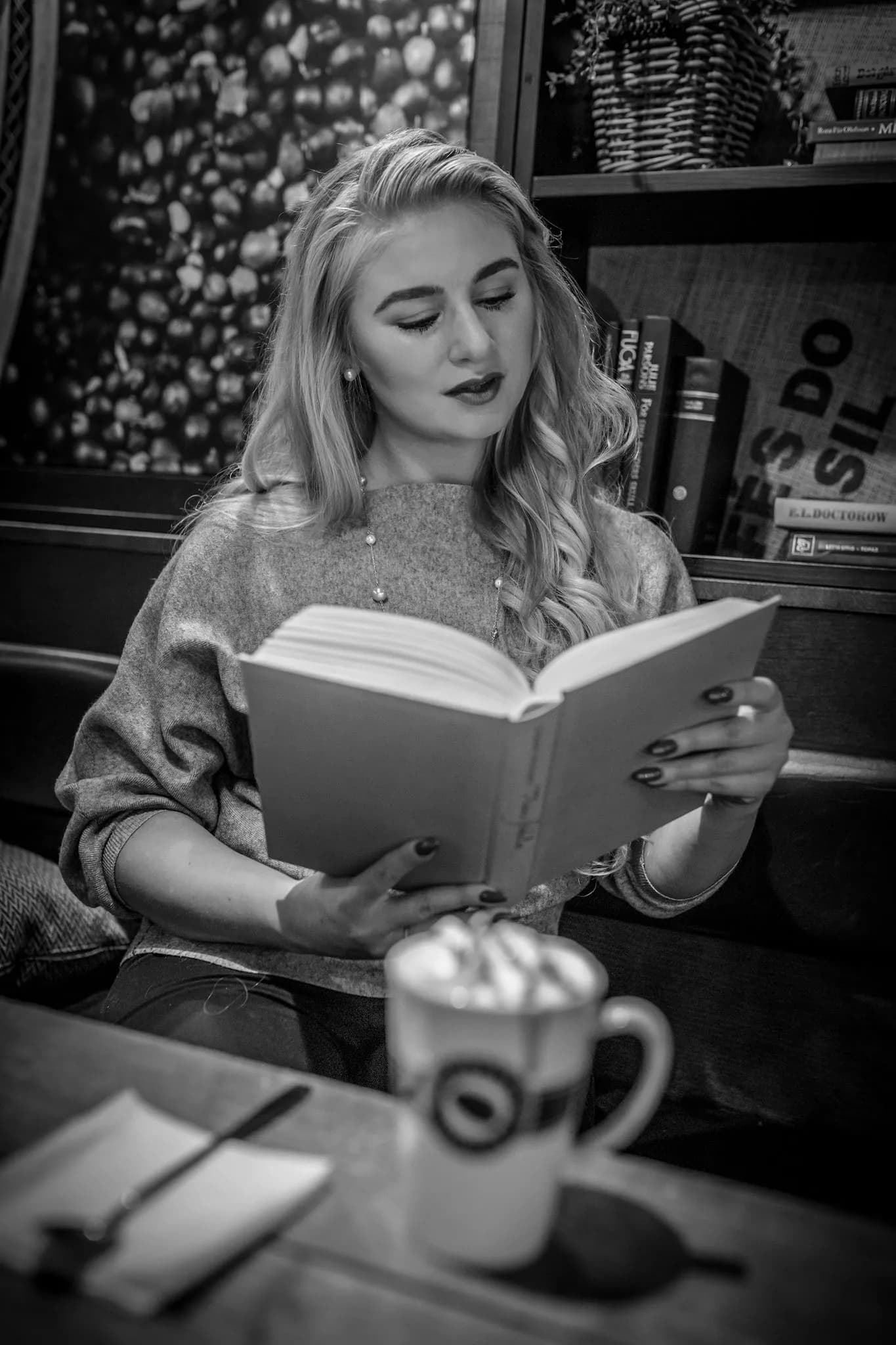 Emily is sitting in a cozy cafe, reading a book with a cup of coffee on the table.