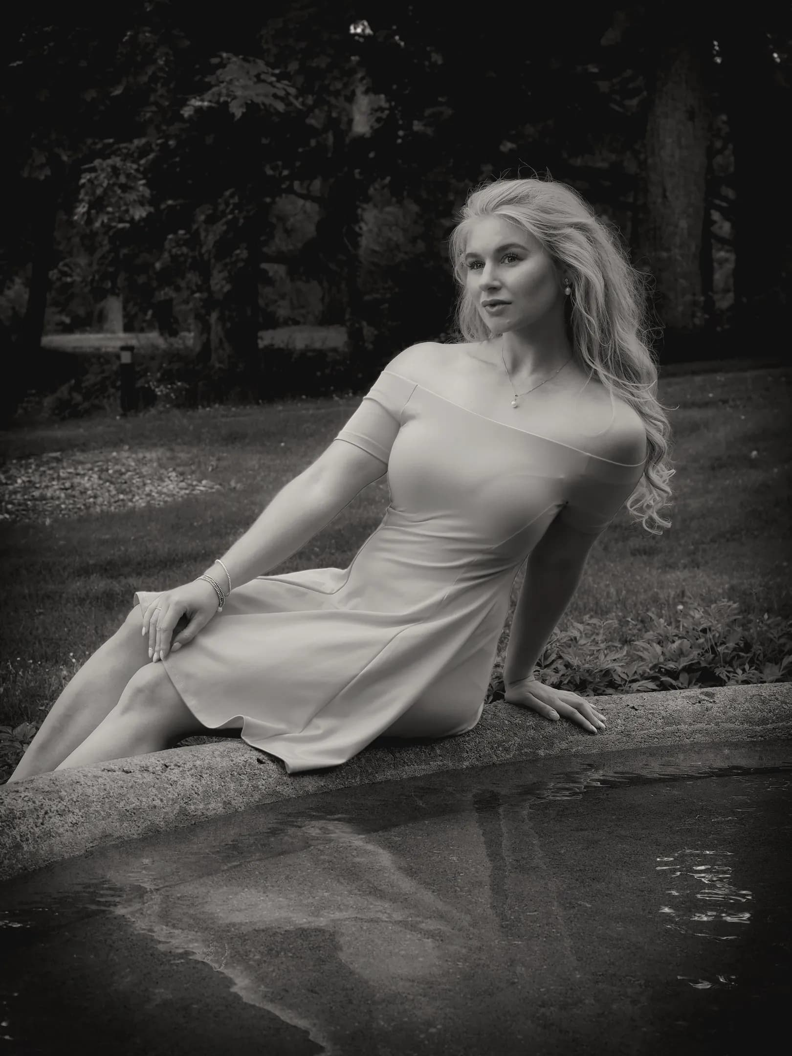 Emily sitting by a pond in a garden, wearing an off-shoulder dress.